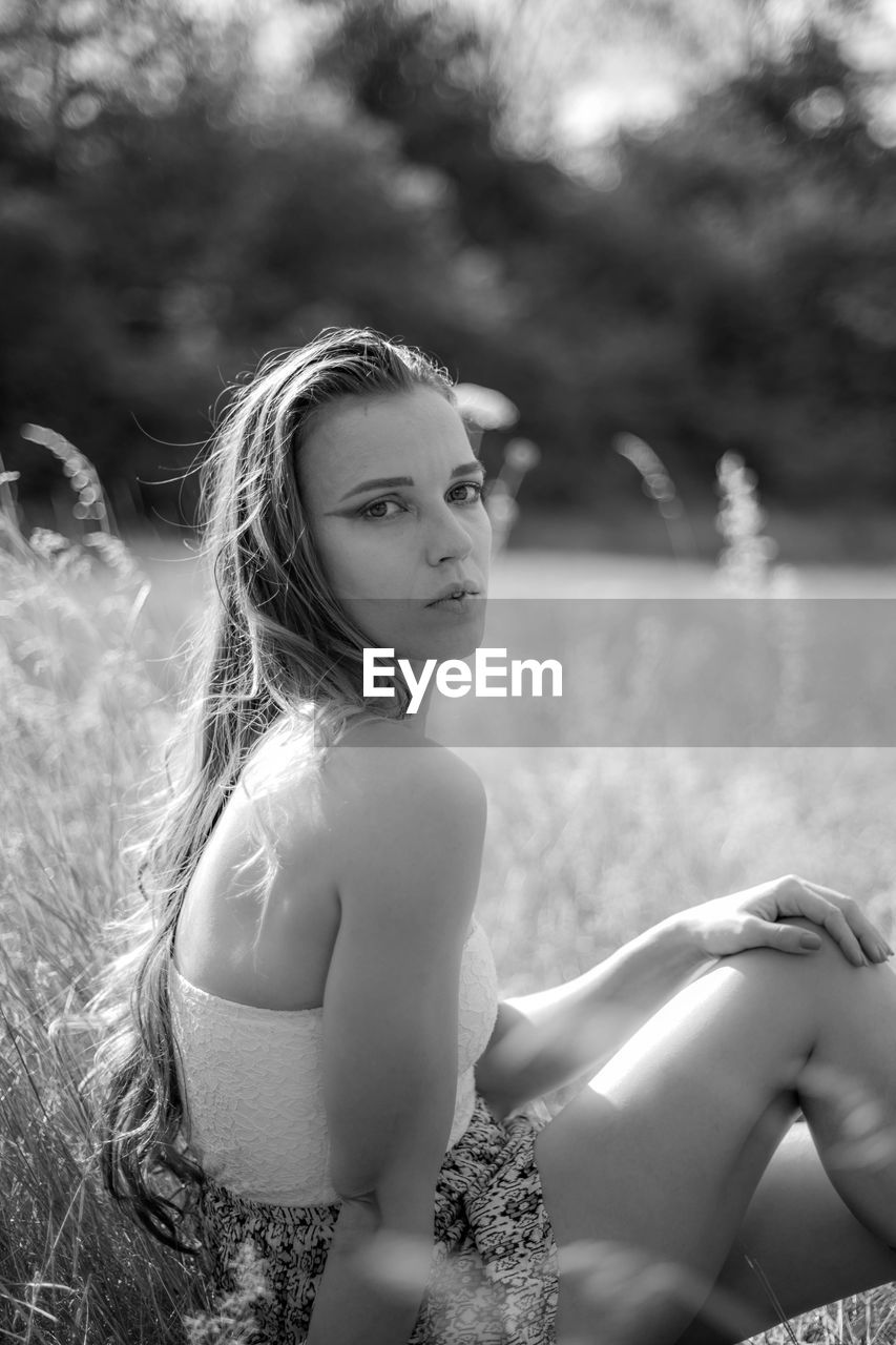 Portrait of a beautiful young woman with dreamy eyes and dress sitting in grass 