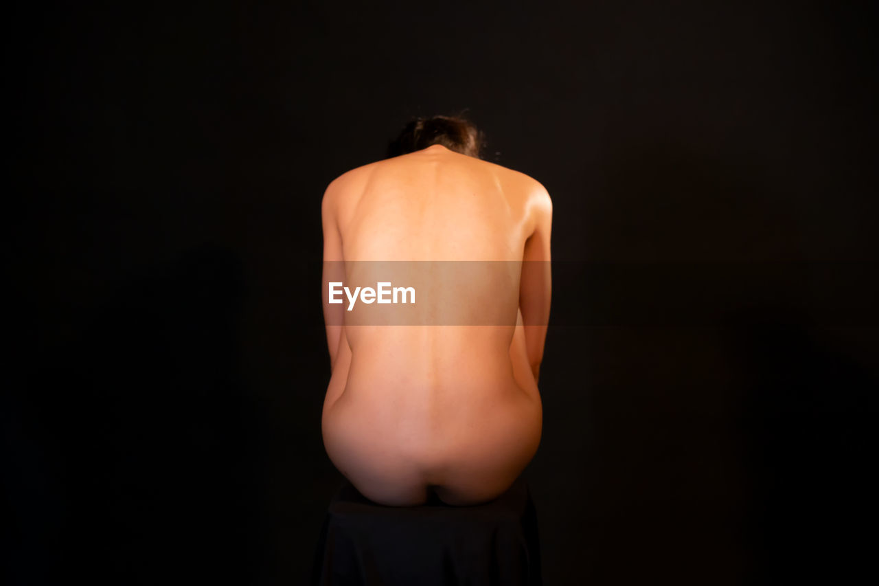 Rear view of naked woman against black background