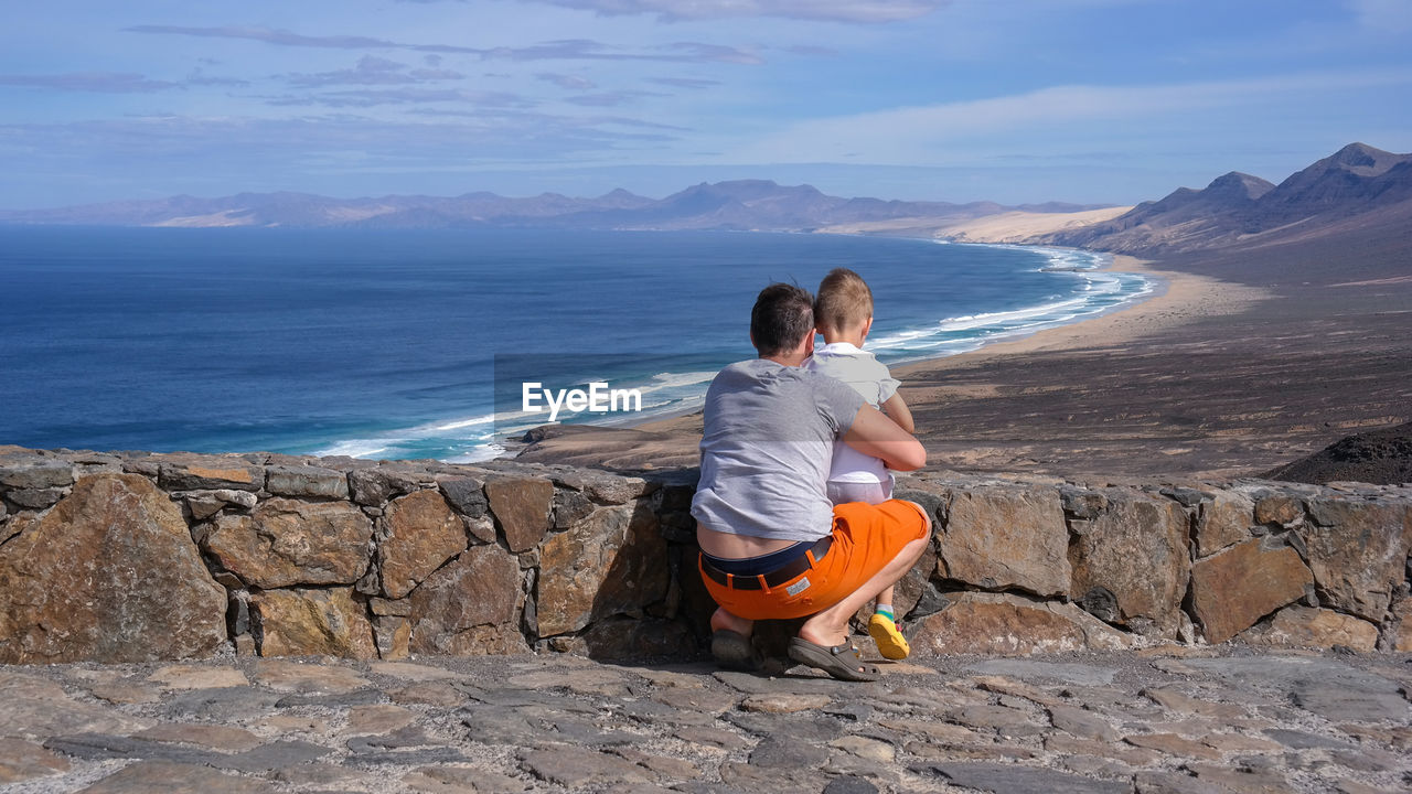 Rear view of father and son at beach against sky