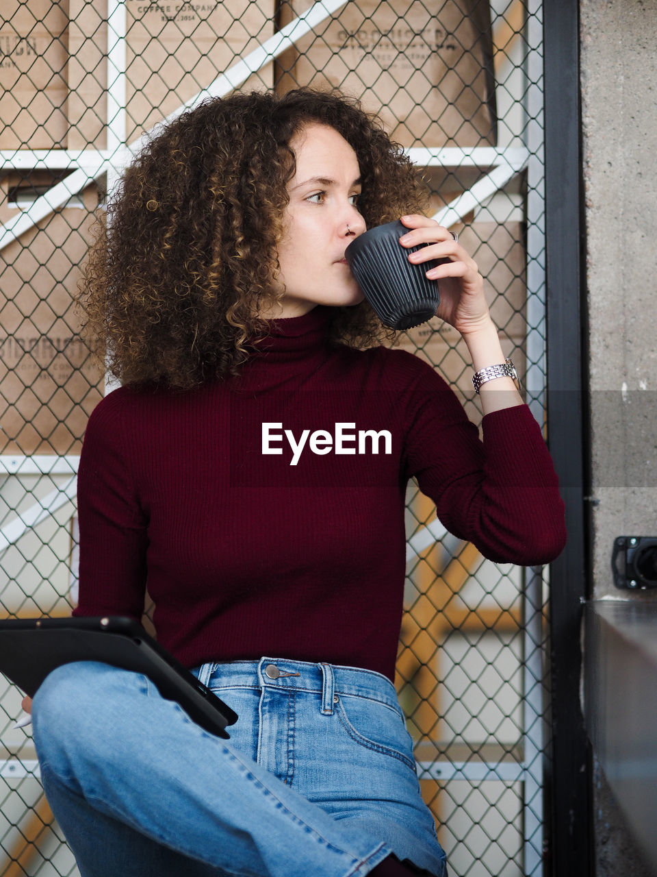 Portrait of young beautiful curly brunette woman drinking coffee while sitting at table in cafe.