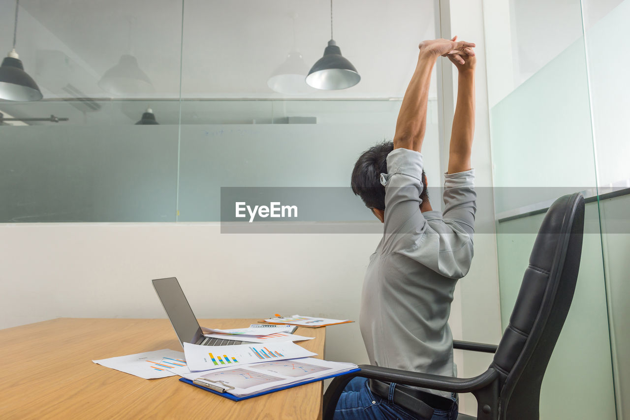 rear view of woman using digital tablet while sitting on table in office