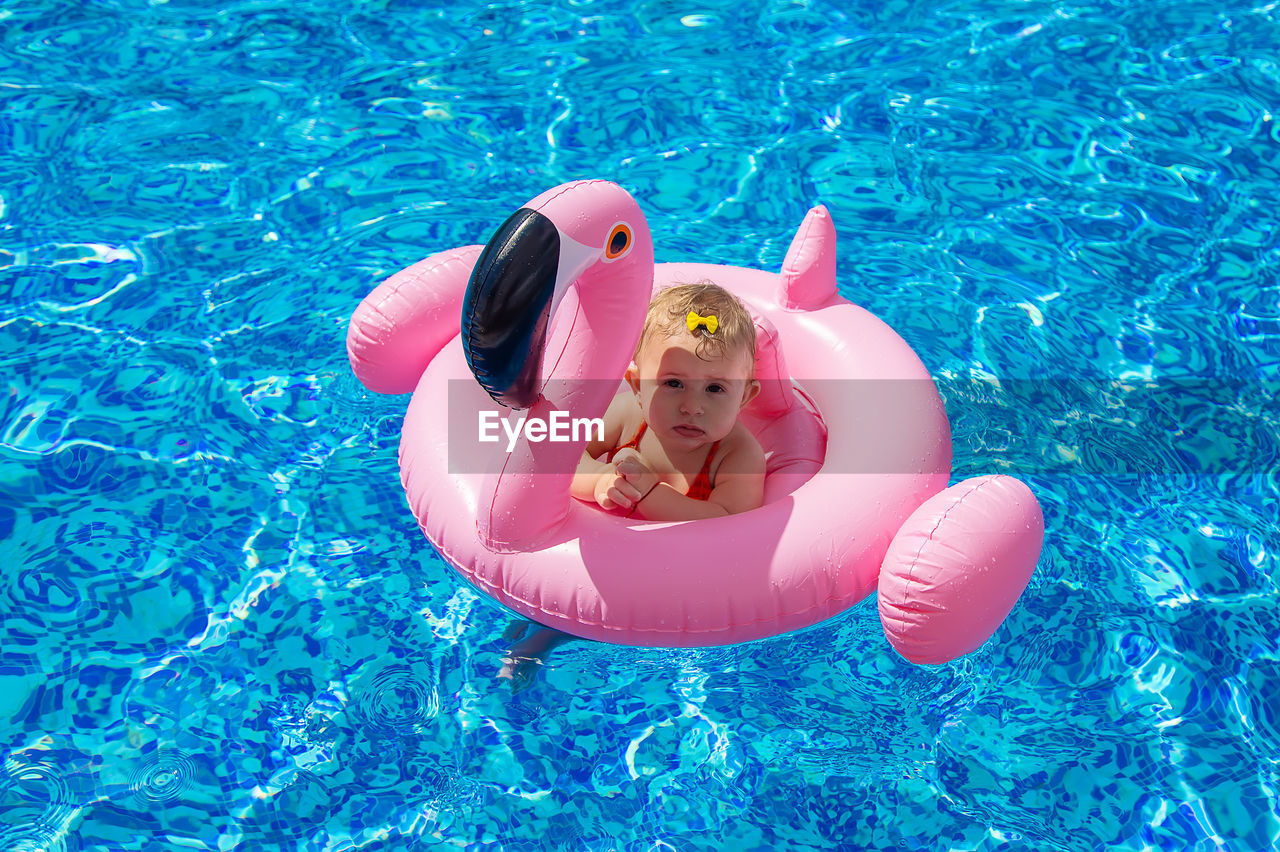Cute girl sitting on pool raft in swimming pool