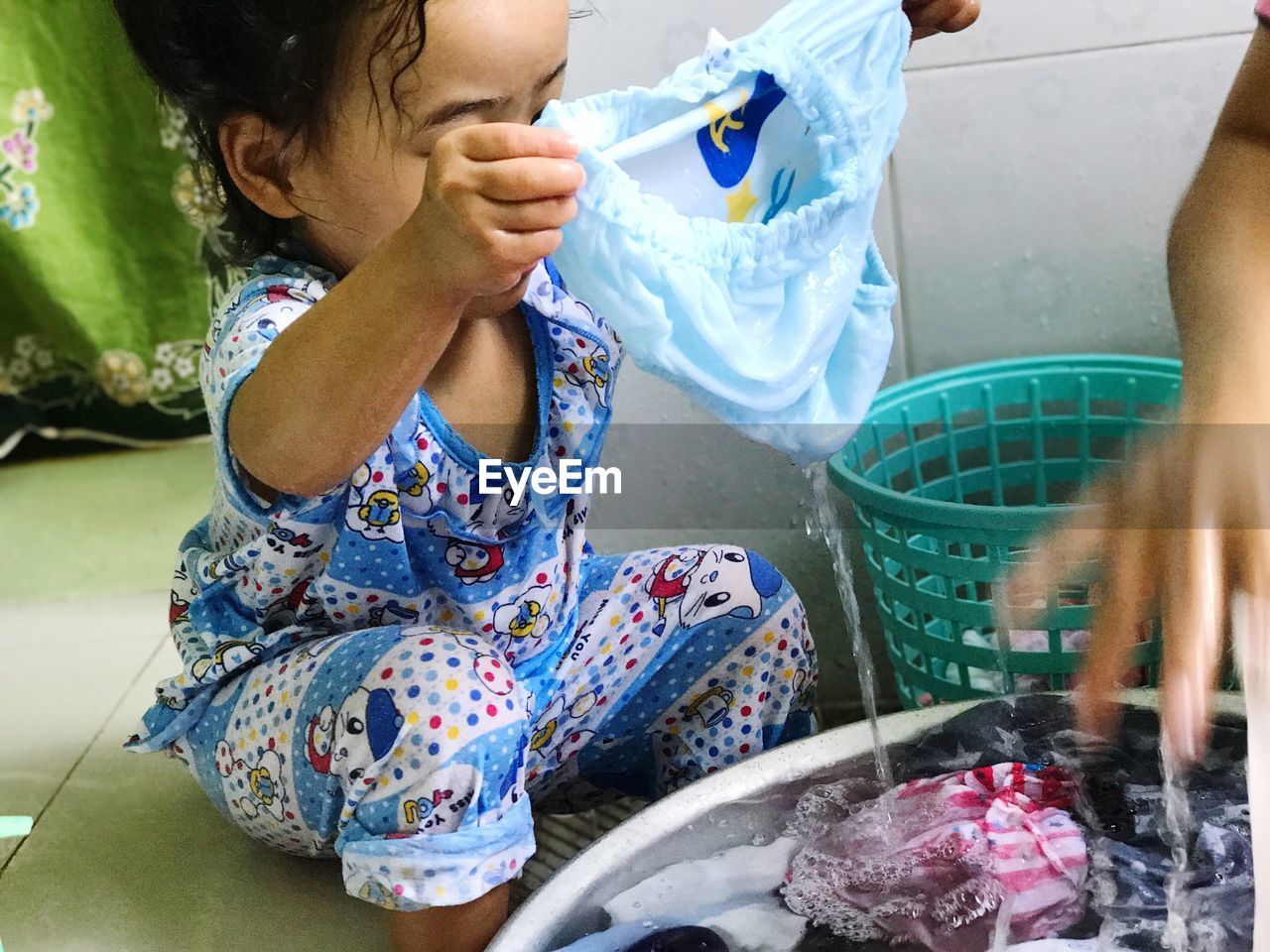 Close-up of girl assisting mother washing clothes