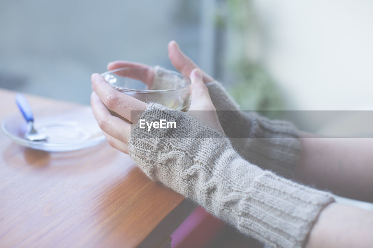 Cropped image of woman wearing mitten holding tea cup at cafe