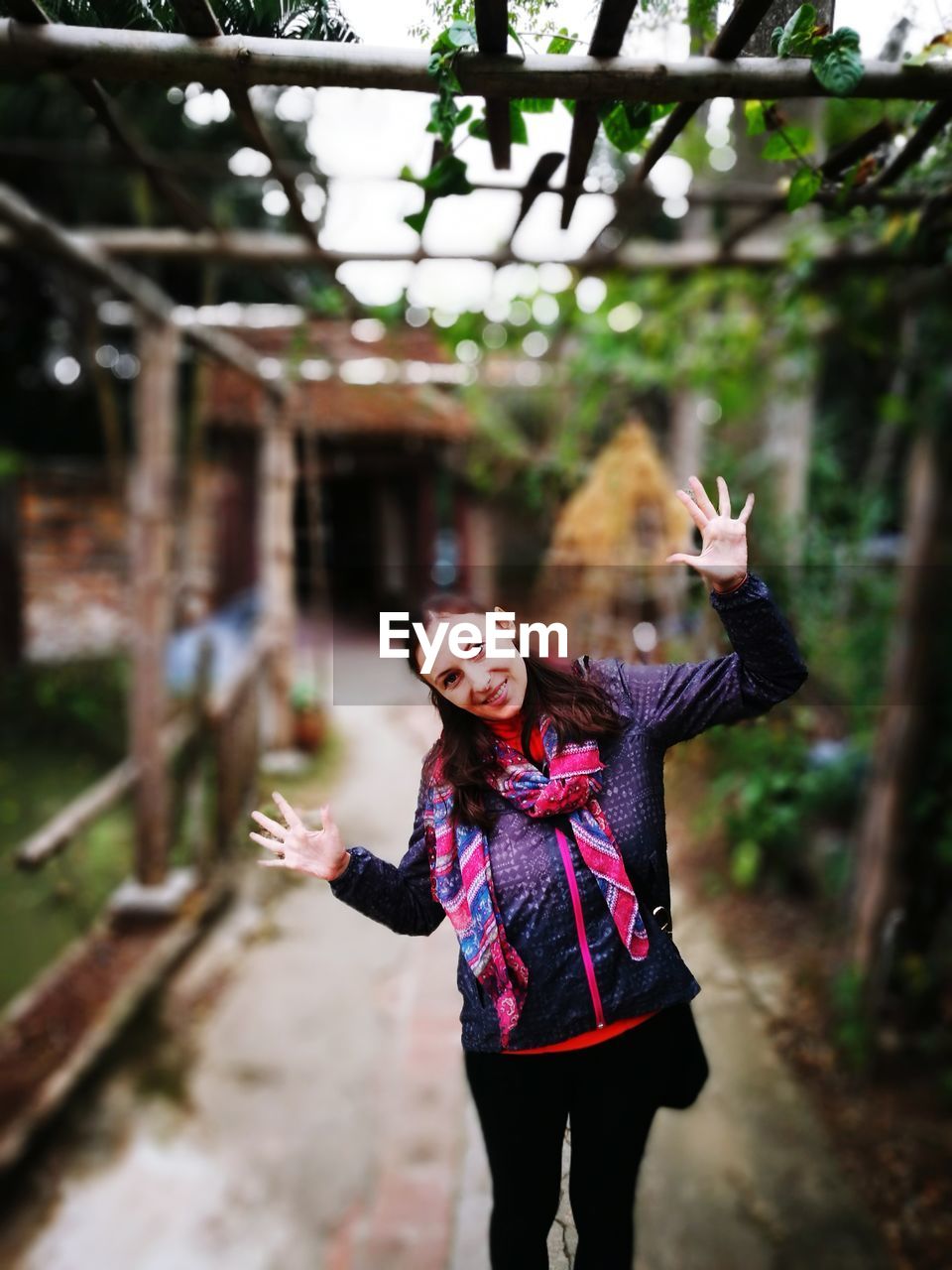 Portrait of smiling young woman gesturing while standing outdoors