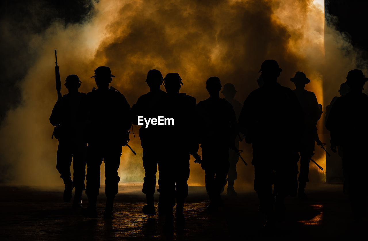 Silhouette army soldiers with guns walking by towards smoke 