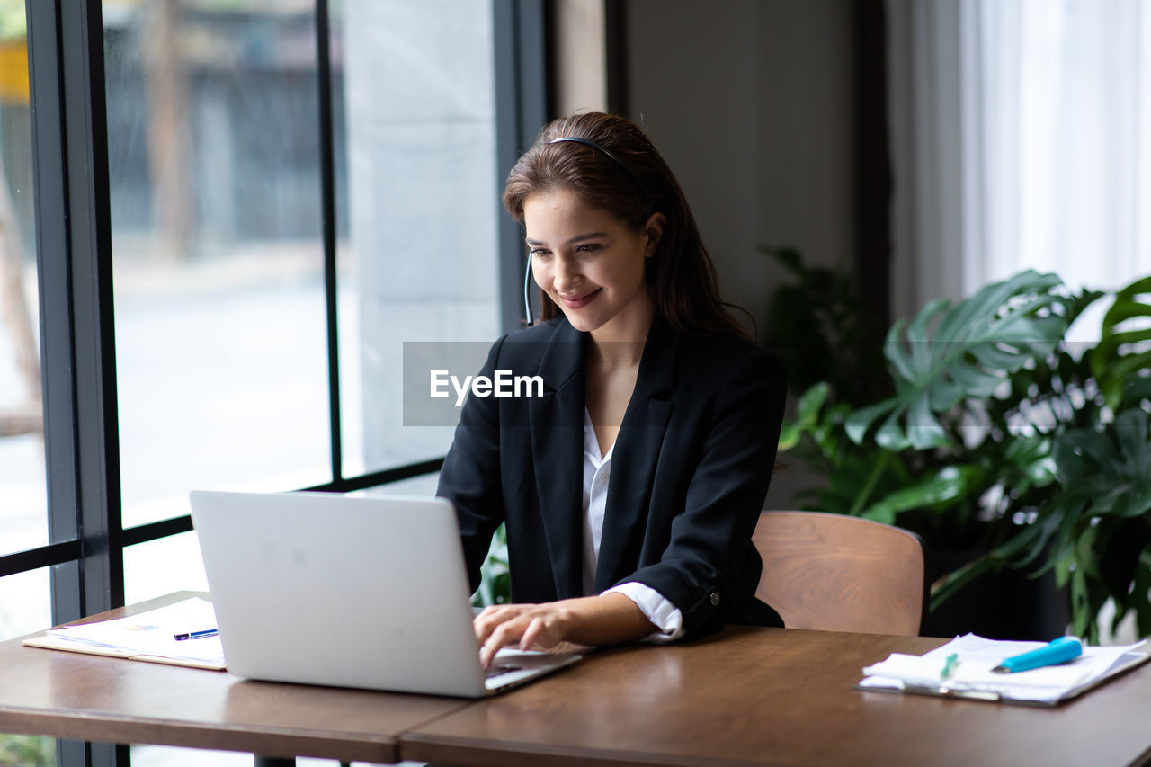 YOUNG WOMAN USING MOBILE PHONE WHILE SITTING AT TABLE