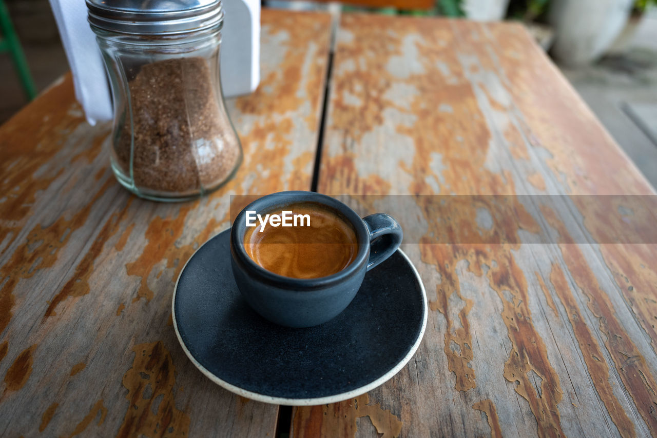 food and drink, coffee, drink, table, coffee cup, mug, cup, refreshment, wood, cafe, crockery, food, still life, indoors, freshness, hot drink, high angle view, no people, saucer, kitchen utensil, spoon, eating utensil, coffee shop, day, focus on foreground, close-up, restaurant