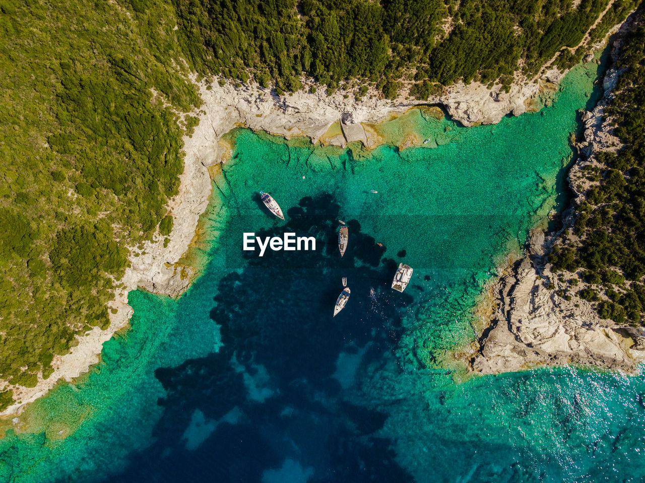 Scenic view of sea and rocks in blue bay with sailing yachts at anchor.
