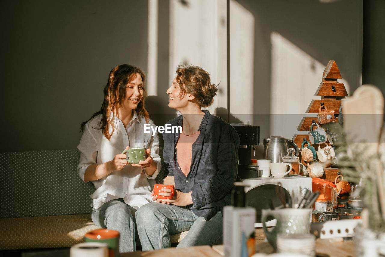 Two female friends enjoying morning coffee in cozy home kitchen