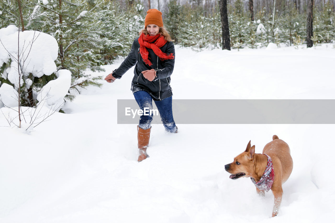 Young woman is playing with her dog on a walk in winter coniferous forest.