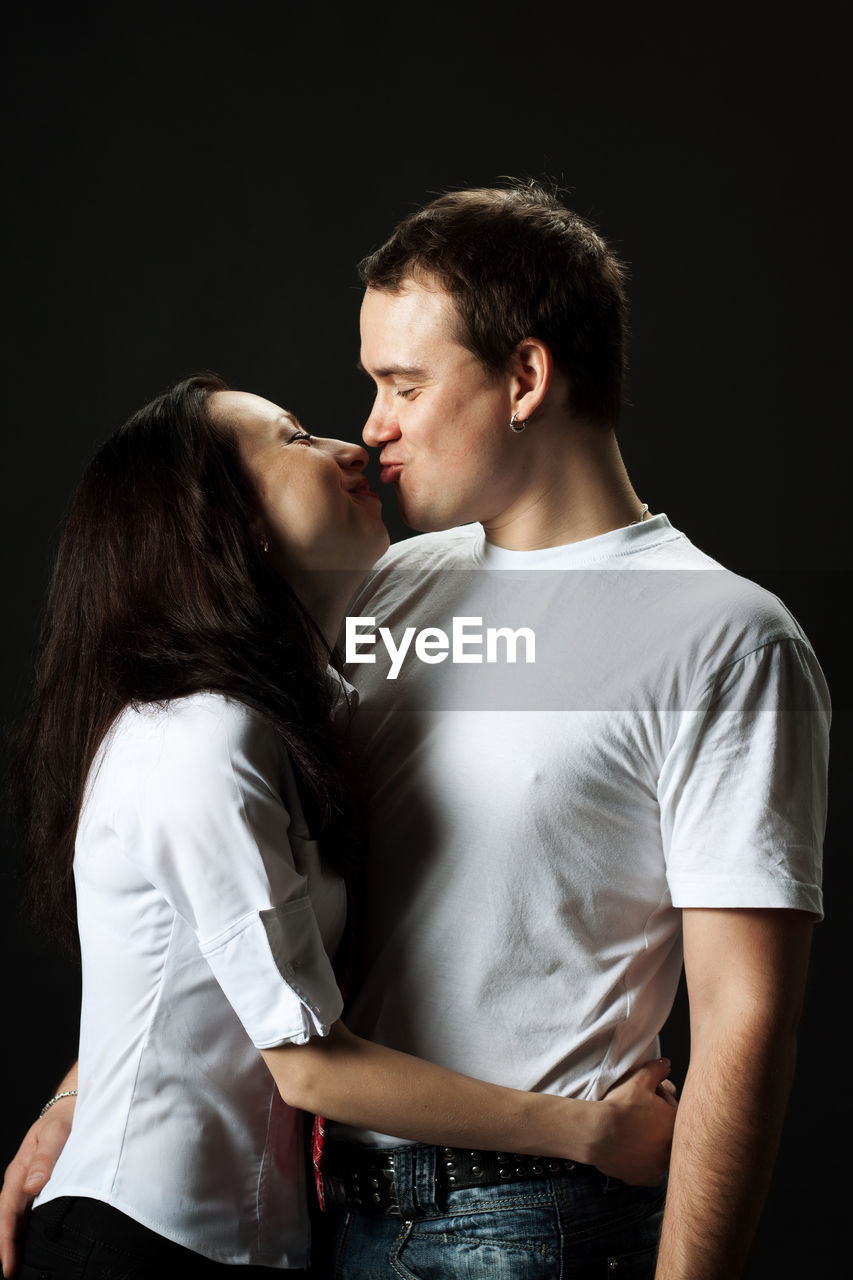 Romantic young couple kissing against black background