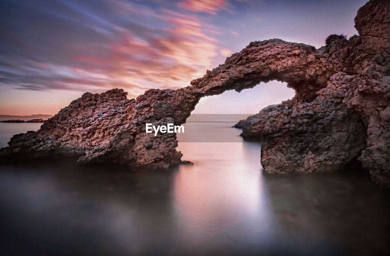 Rock formation in sea against sky during sunset