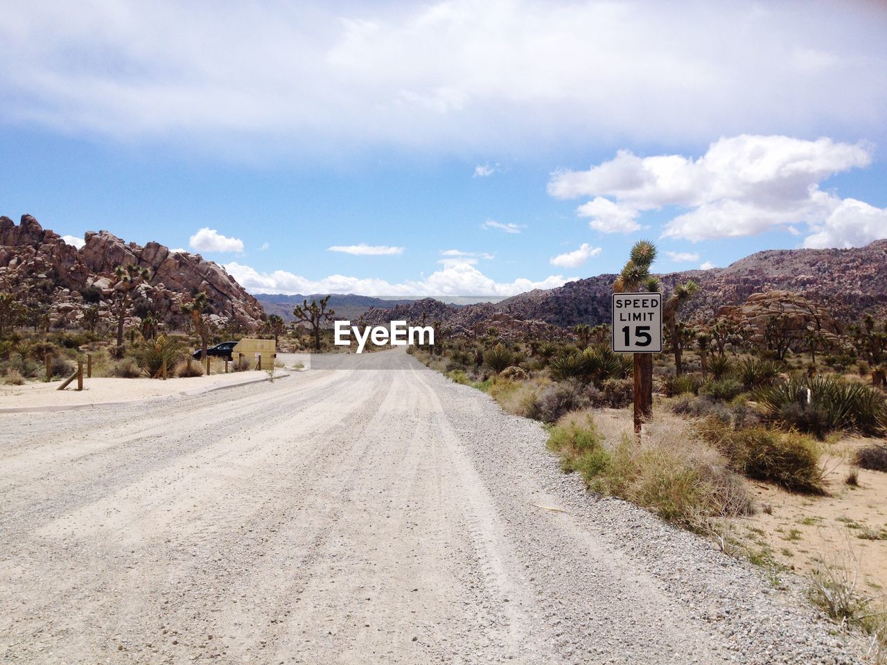 Speed limit sign by road leading towards mountains against sky