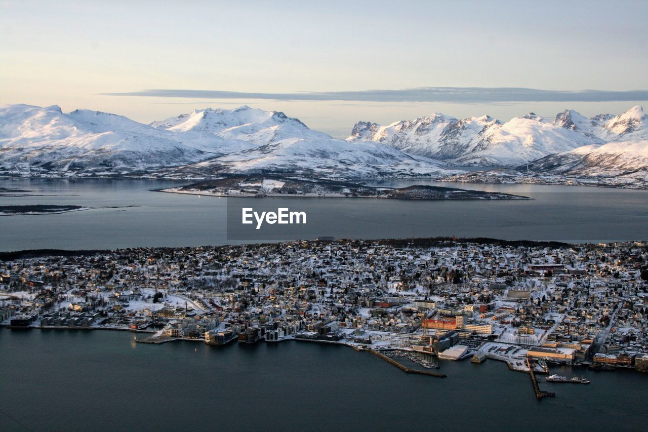 Aerial view of city by sea against snowcapped mountains