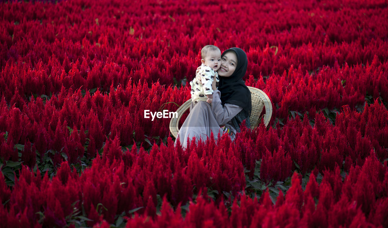 Mom and daughter on red flowering plants on field