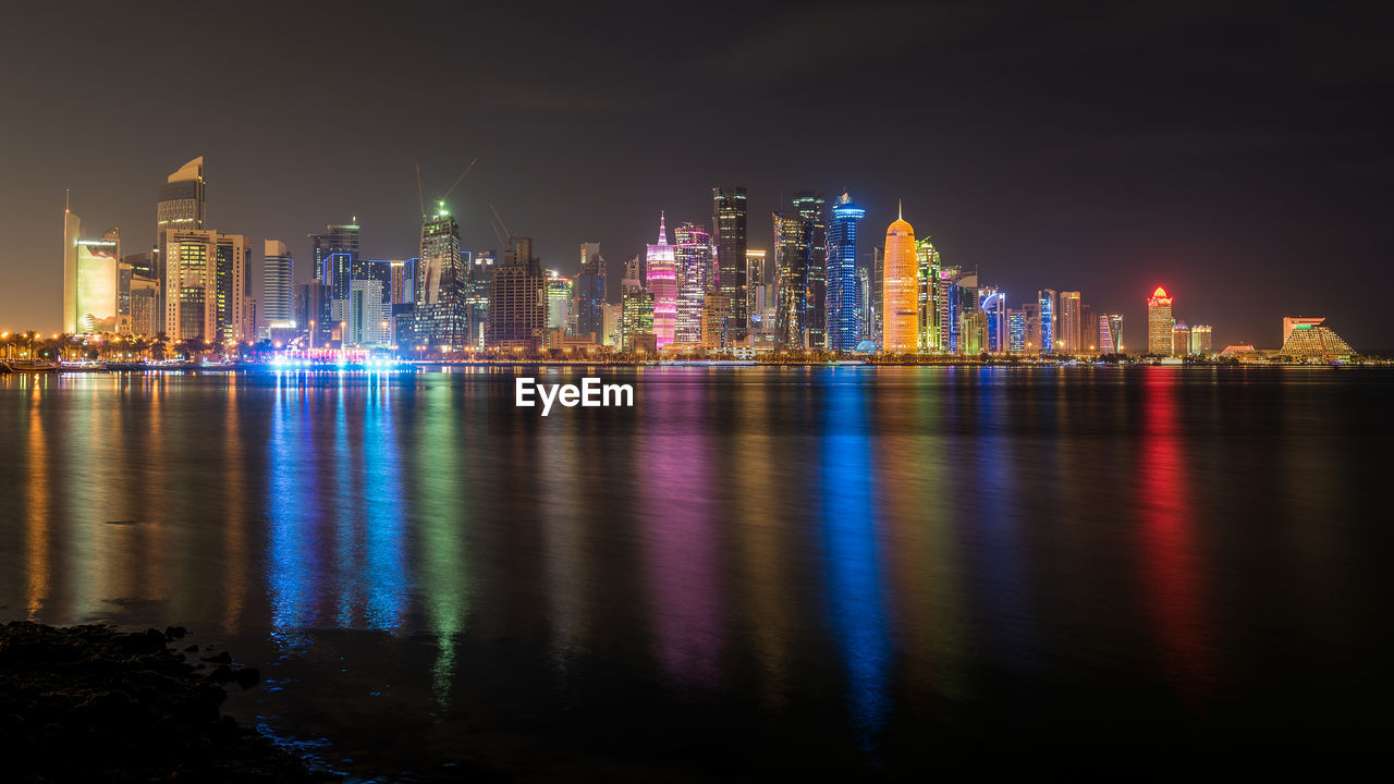 Illuminated city by sea against sky at night