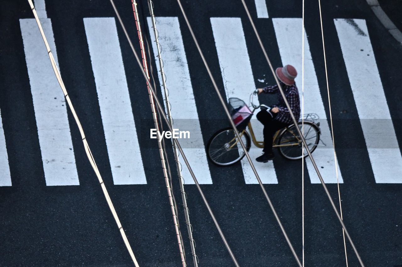 High angle view of electricity cable in front of woman cycling on zebra crossing