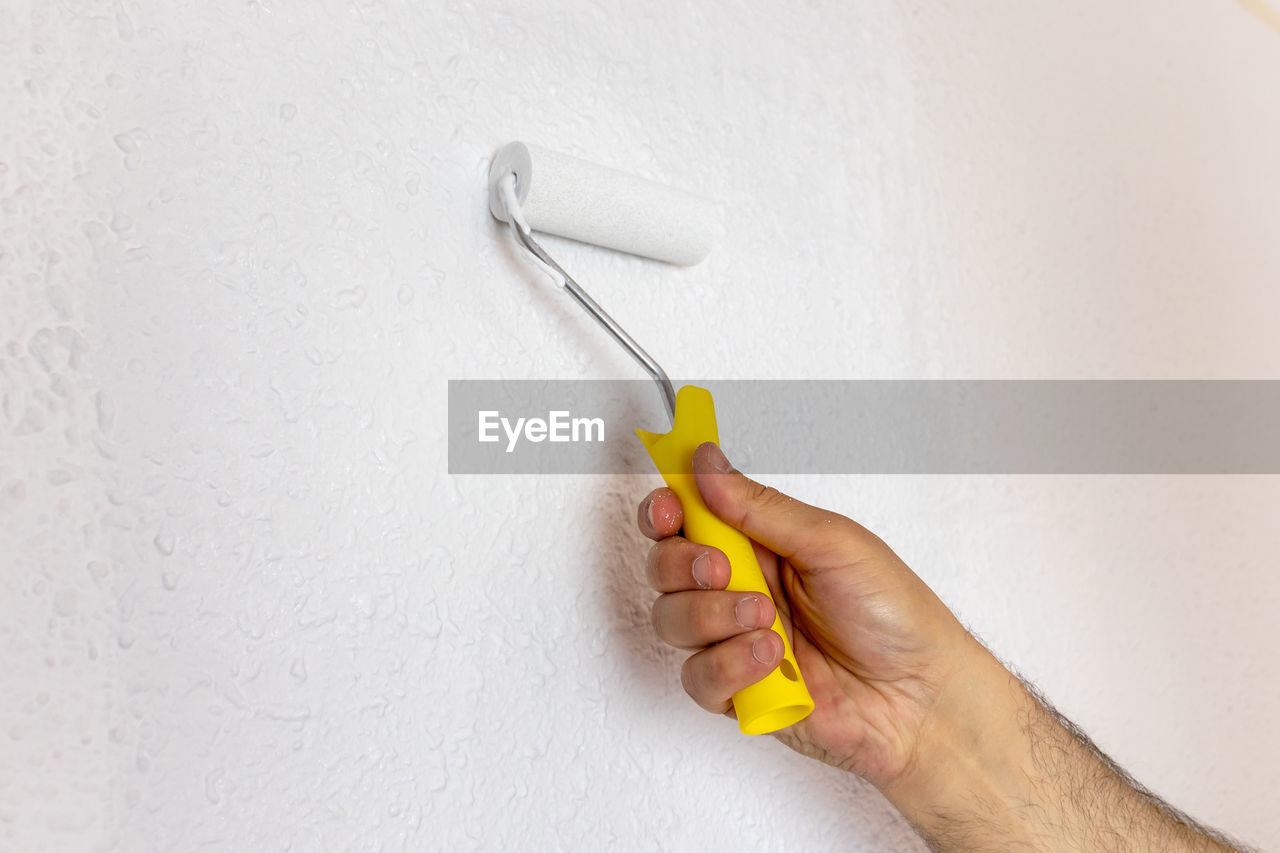 cropped hand holding dental equipment against white wall