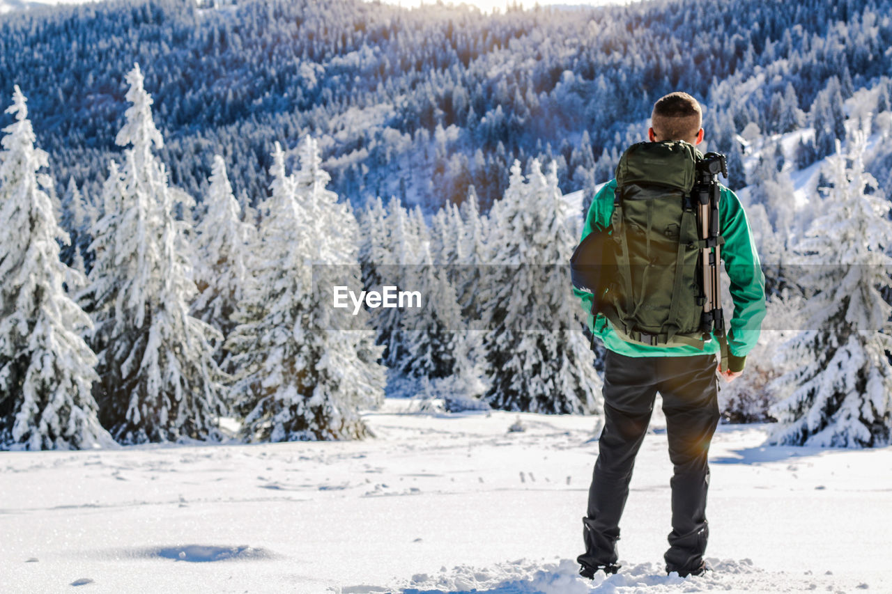 REAR VIEW OF MAN STANDING ON SNOW