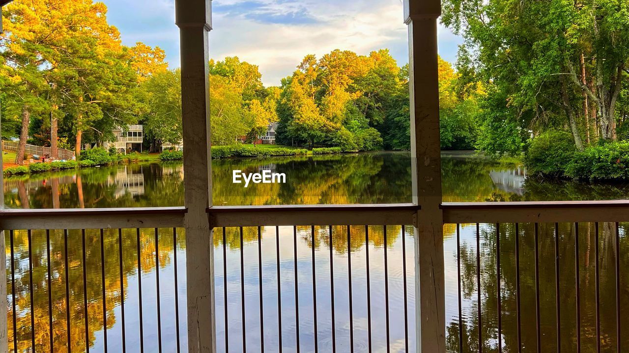 reflection, tree, plant, water, nature, lake, beauty in nature, sunlight, autumn, sky, scenics - nature, no people, architecture, tranquility, leaf, outdoors, cloud, environment, day, tranquil scene, green, landscape, growth, land, built structure, forest, yellow, building, non-urban scene, garden, window, idyllic, travel destinations, plant part, travel, flower