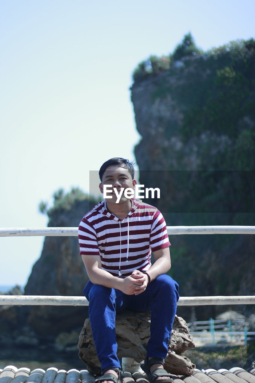 Portrait of smiling young man sitting on rock