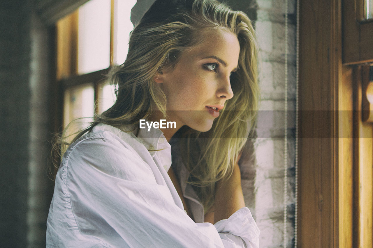 SIDE VIEW OF WOMAN LOOKING THROUGH WINDOW