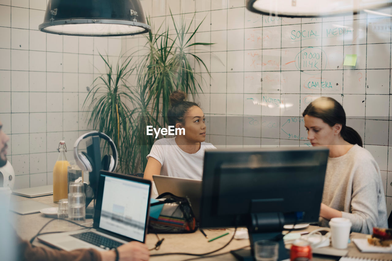 Multi-ethnic female hackers working at desk in creative office seen through window