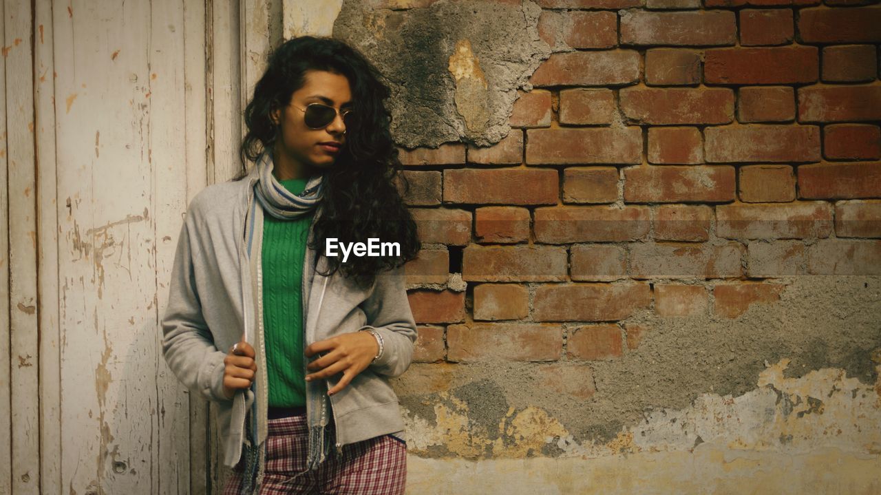 Young woman standing against brick wall