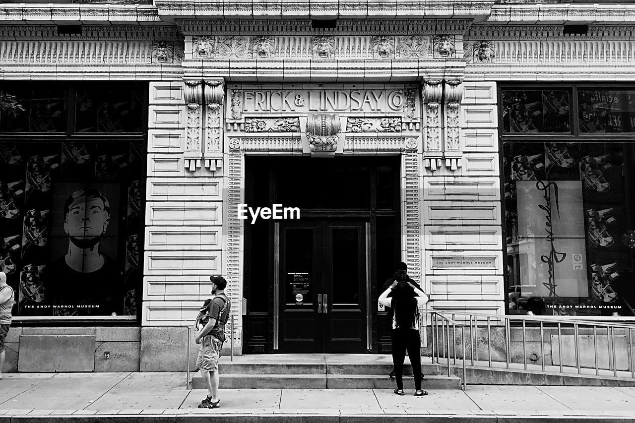 REAR VIEW OF MAN AND WOMAN WALKING AT BUILDING