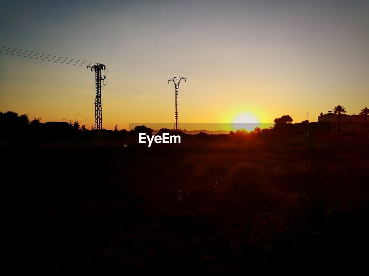 Silhouette electricity pylons on land against sky during sunset