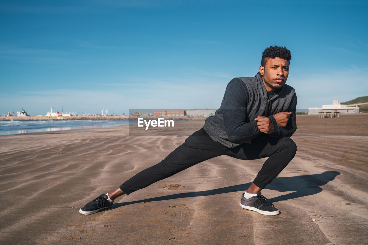 Young man exercising on beach against sky