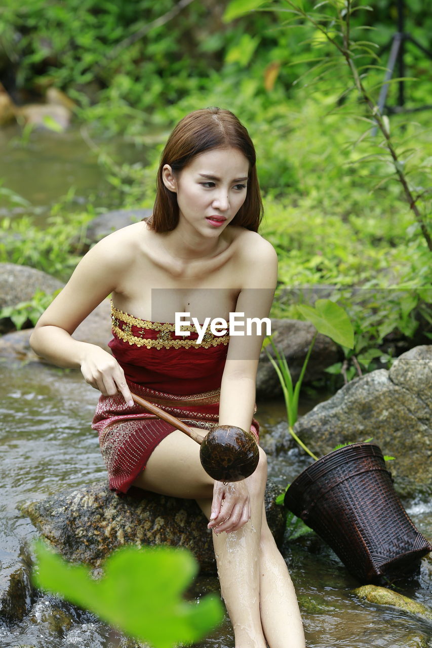 BEAUTIFUL YOUNG WOMAN SITTING AGAINST WATER