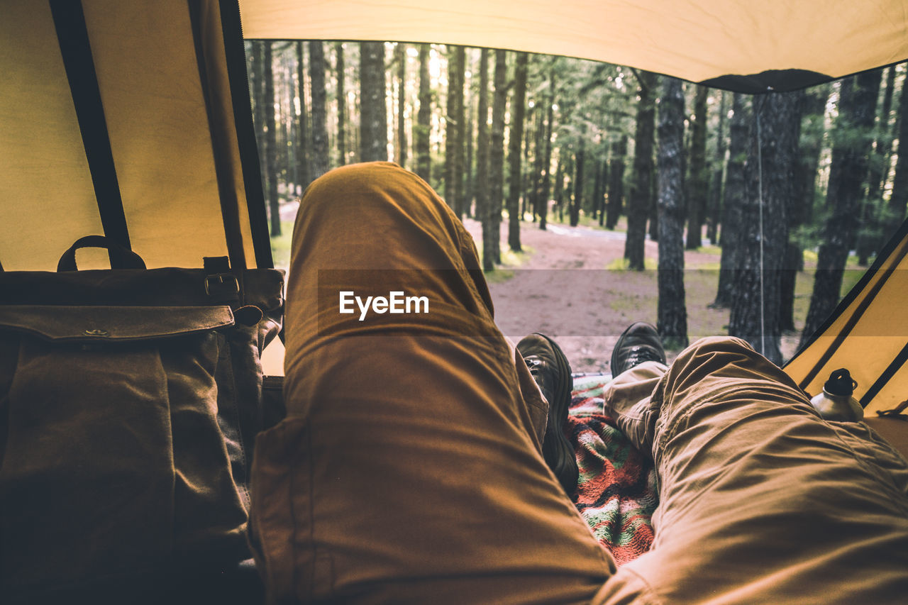 Low section of person relaxing in tent at forest