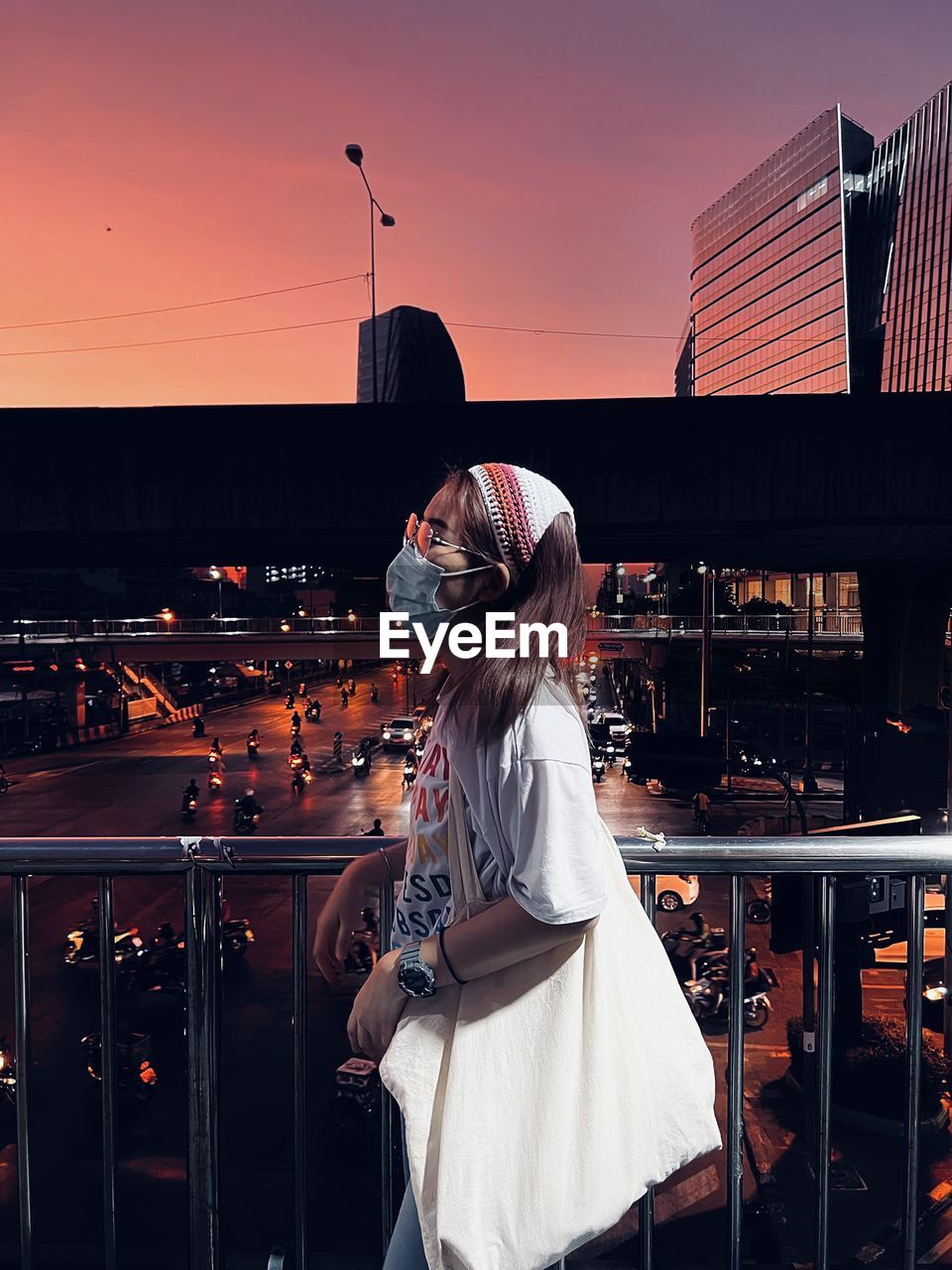 Rear view of young woman standing against buildings during sunset