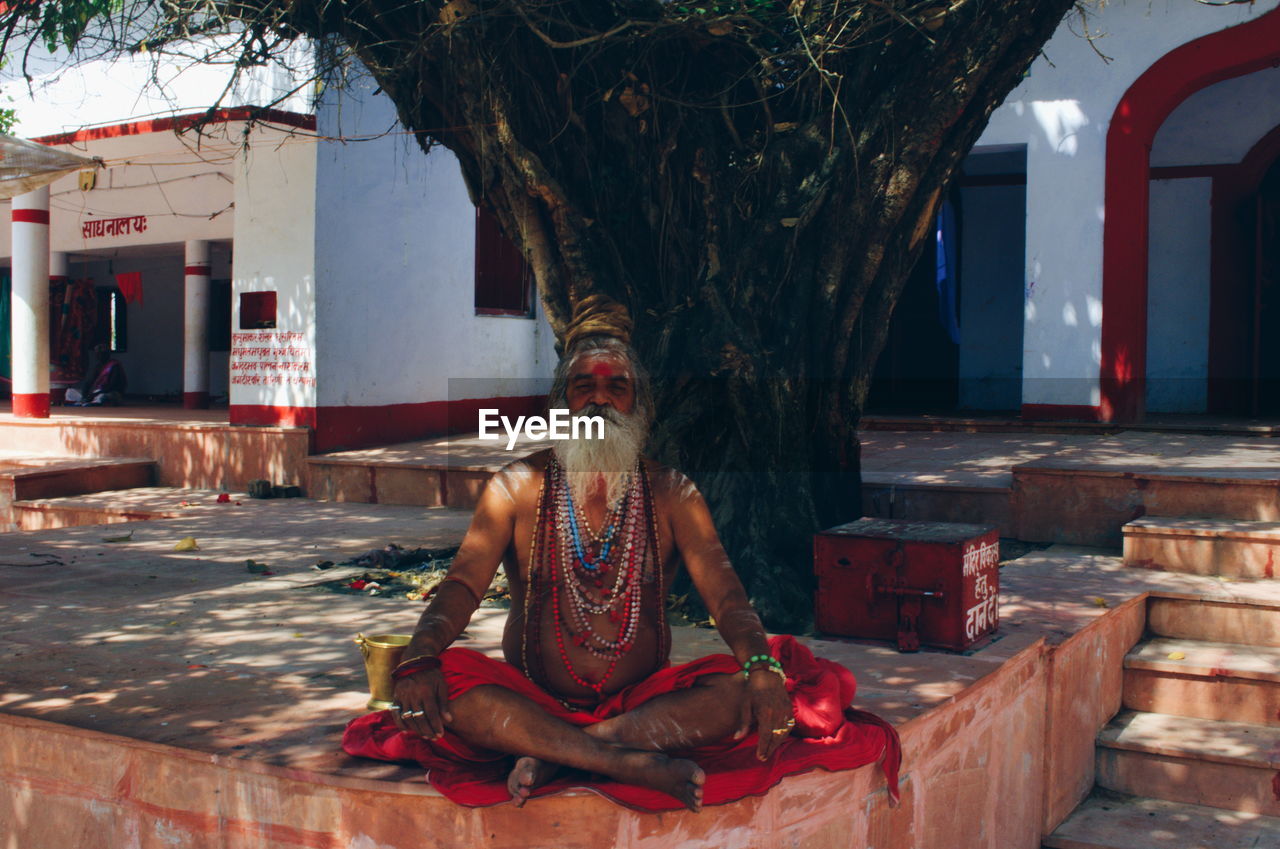 FULL LENGTH OF MAN SITTING ON CROSS AGAINST TREE