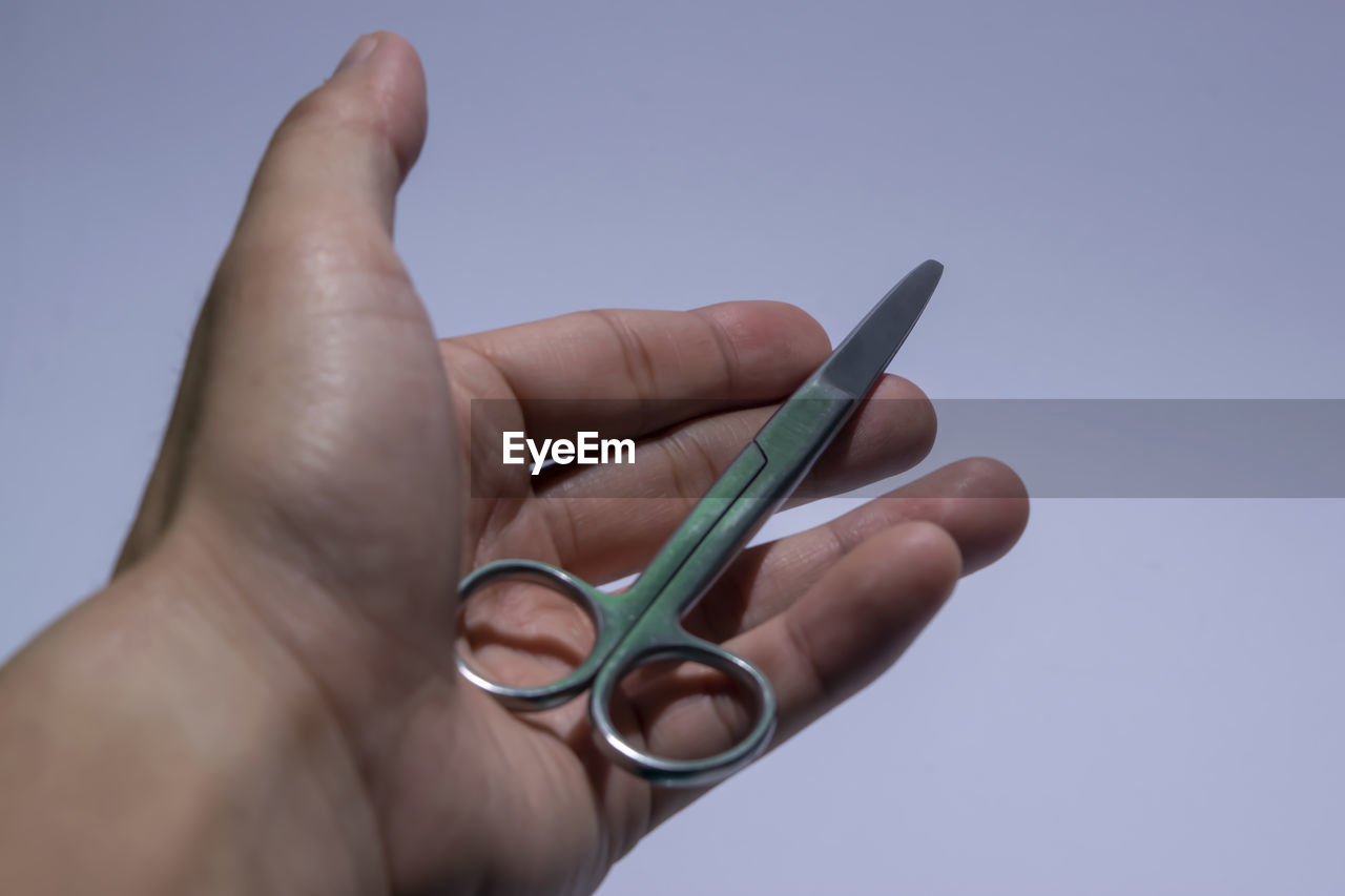 Close-up of hand holding surgical equipment against gray background