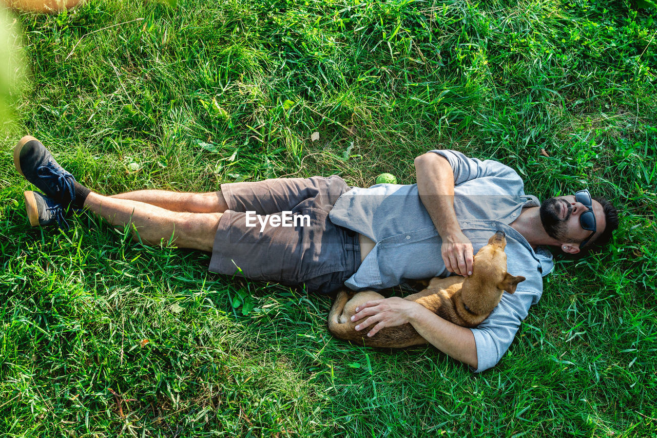 grass, lying down, plant, relaxation, lawn, lying on back, green, nature, men, casual clothing, adult, leisure activity, full length, lifestyles, person, one person, young adult, high angle view, day, field, sleeping, land, outdoors, footwear, clothing, resting, emotion