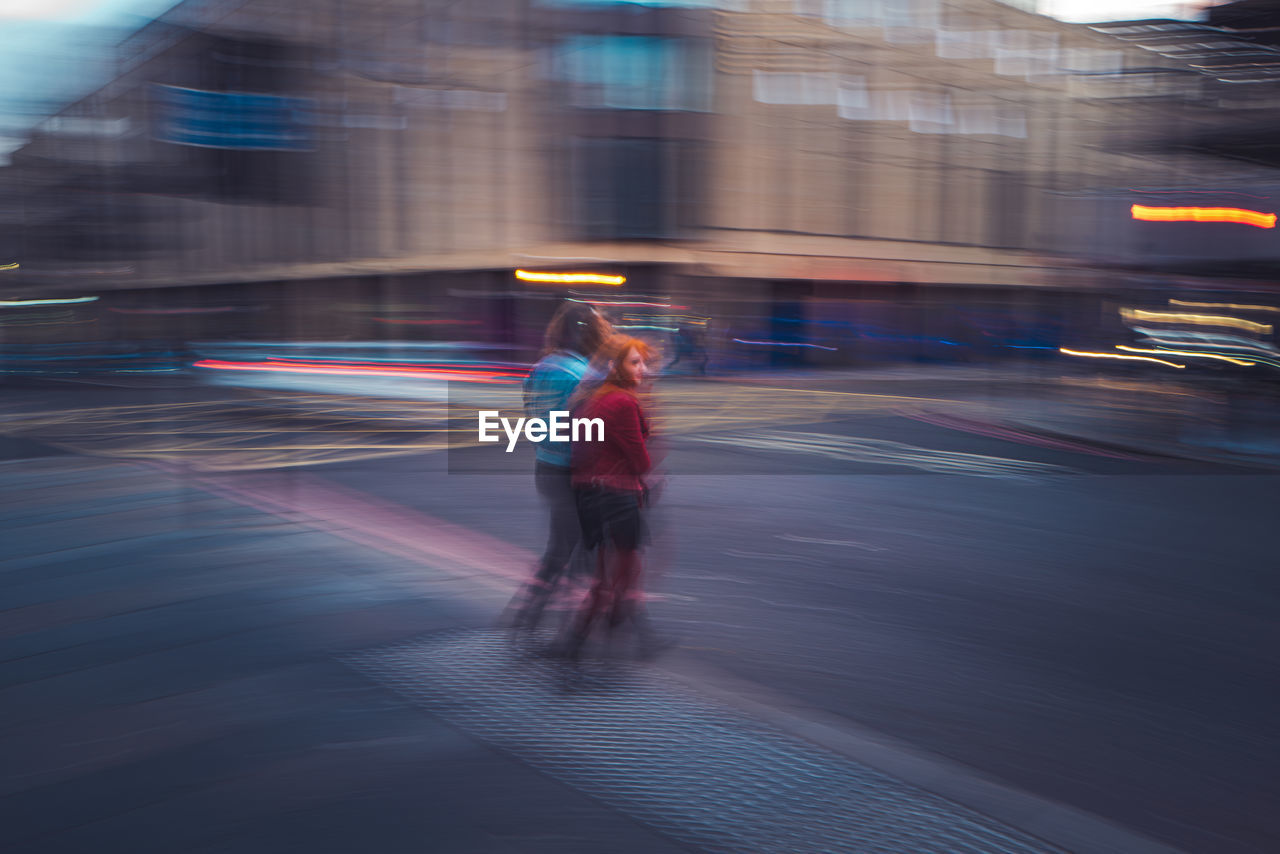 blurred motion, motion, architecture, speed, city, transportation, full length, one person, long exposure, illuminated, street, building exterior, built structure, city life, road, on the move, adult, light trail, night, mode of transportation, light, city street, walking, outdoors, rear view, men, travel, reflection, lifestyles