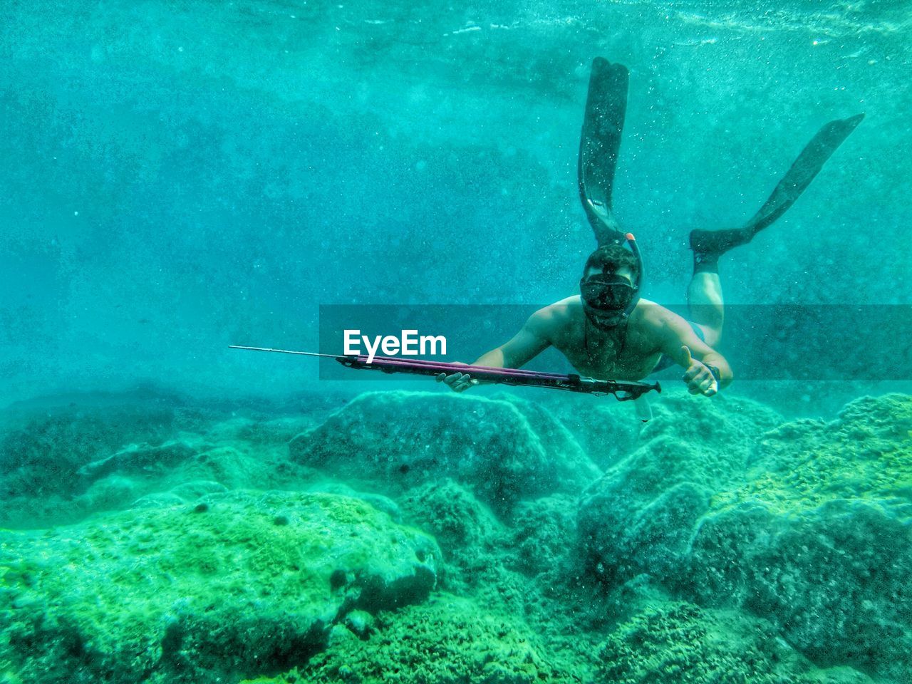 Shirtless man holding harpoon swimming undersea