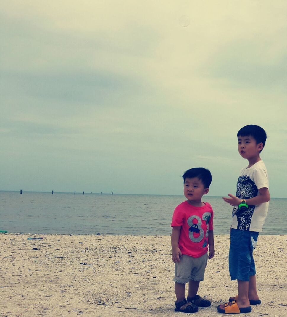 Boys looking away while standing on sand at beach