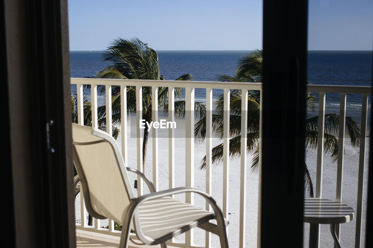 Empty chair on balcony by sea against sky