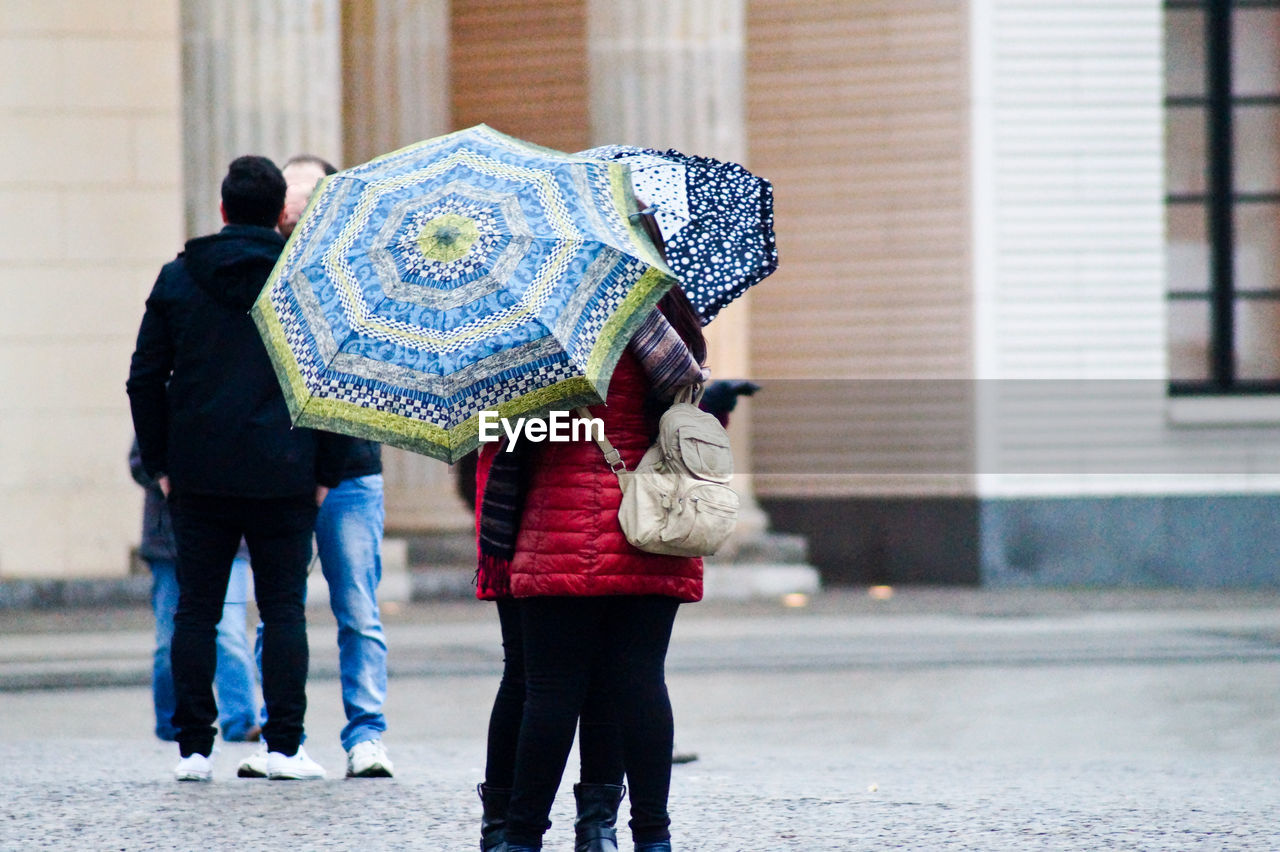 Friends with umbrellas standing on street against building