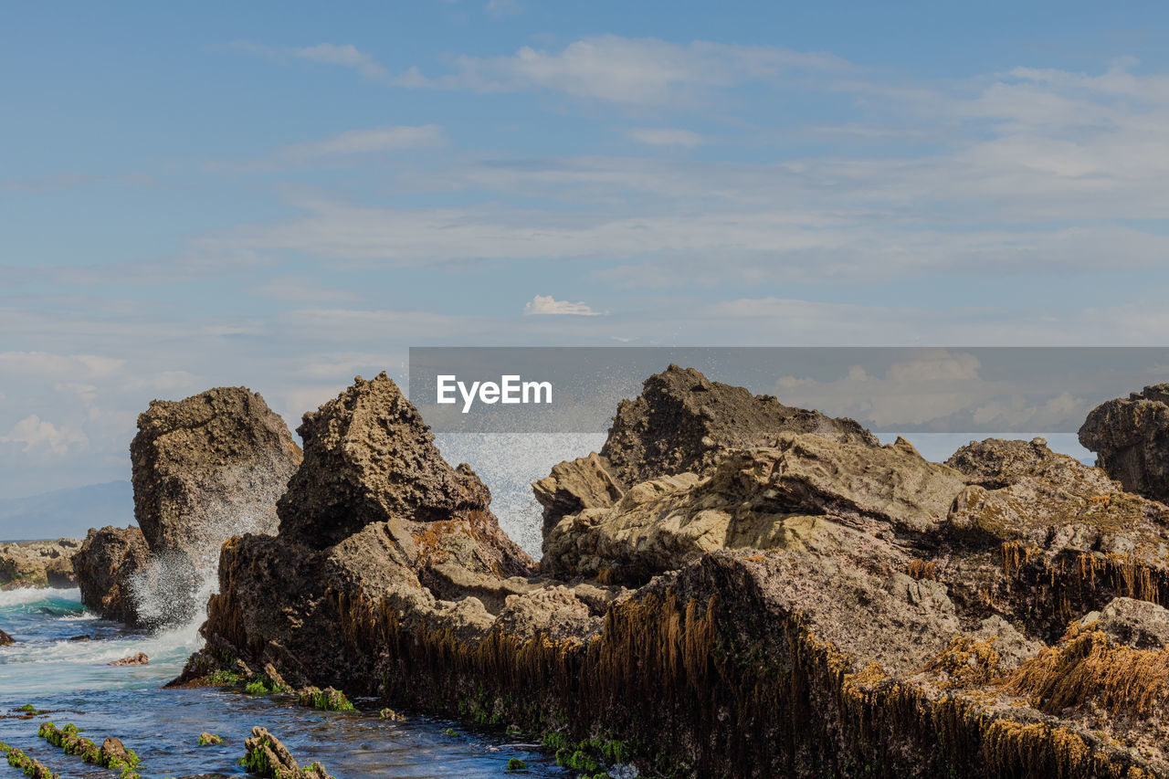 Rock formations on beach against sea wave