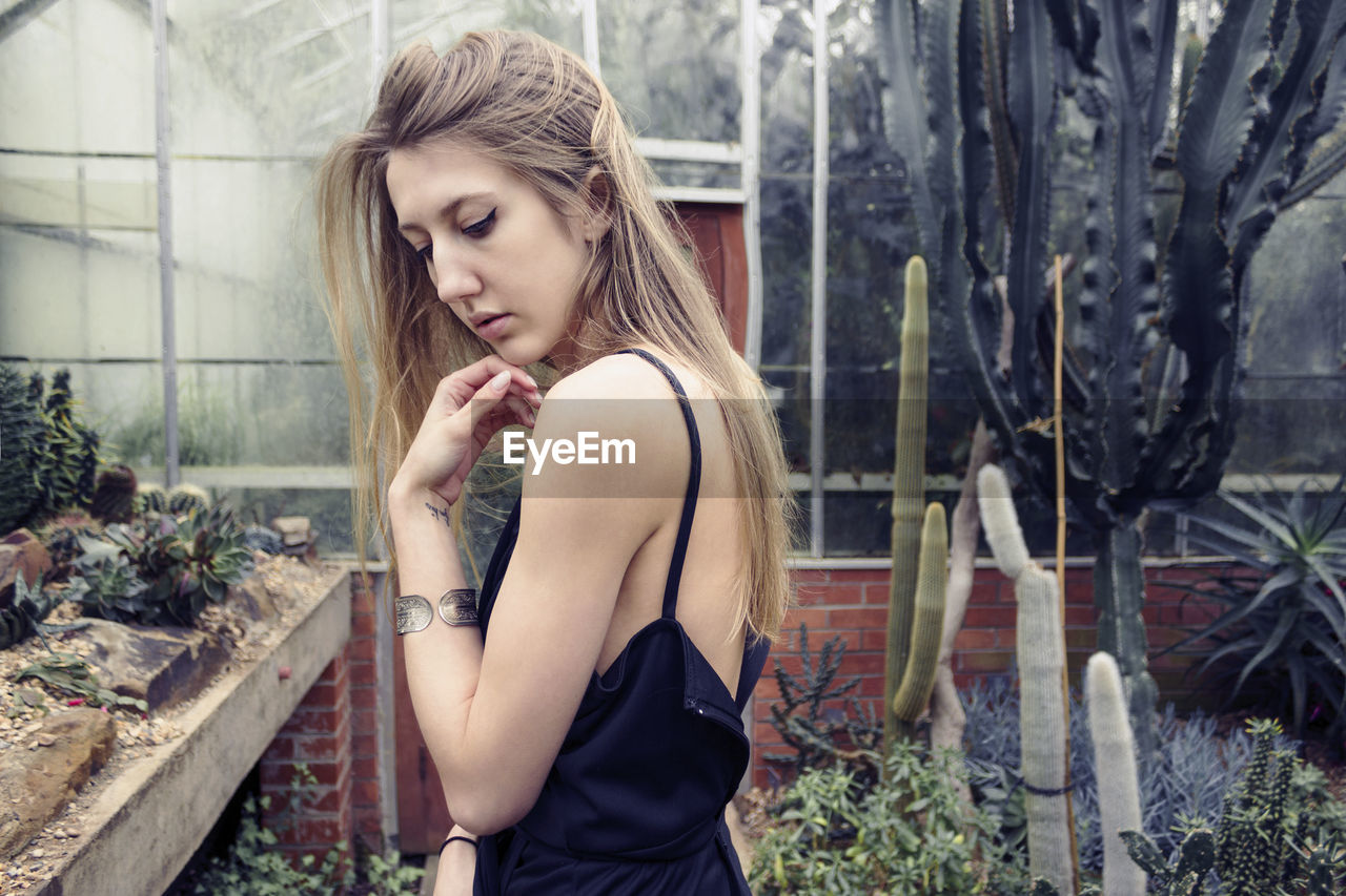 Beautiful young woman looking down while standing in greenhouse