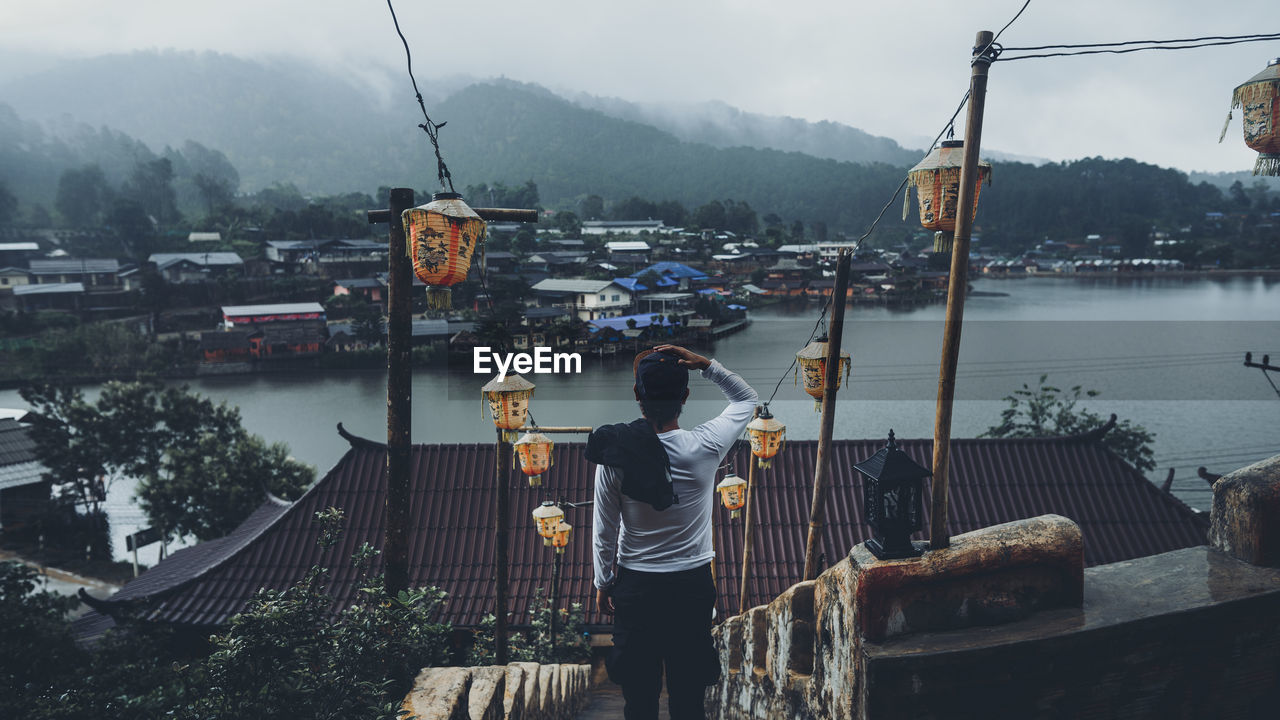 Rear view of man looking at cityscape by river against mountains