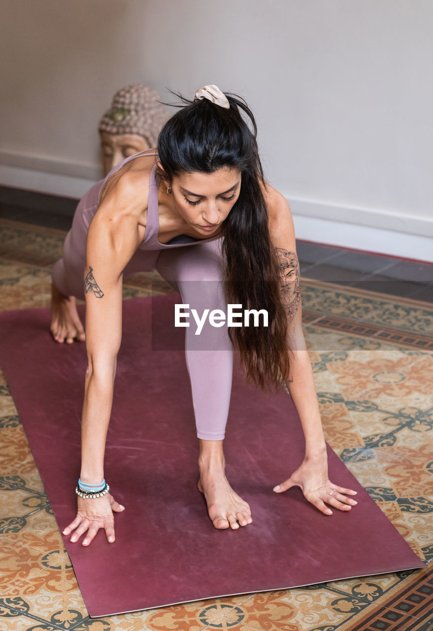 Young flexible ethnic female in sports clothes standing in low lunge pose on mat at home