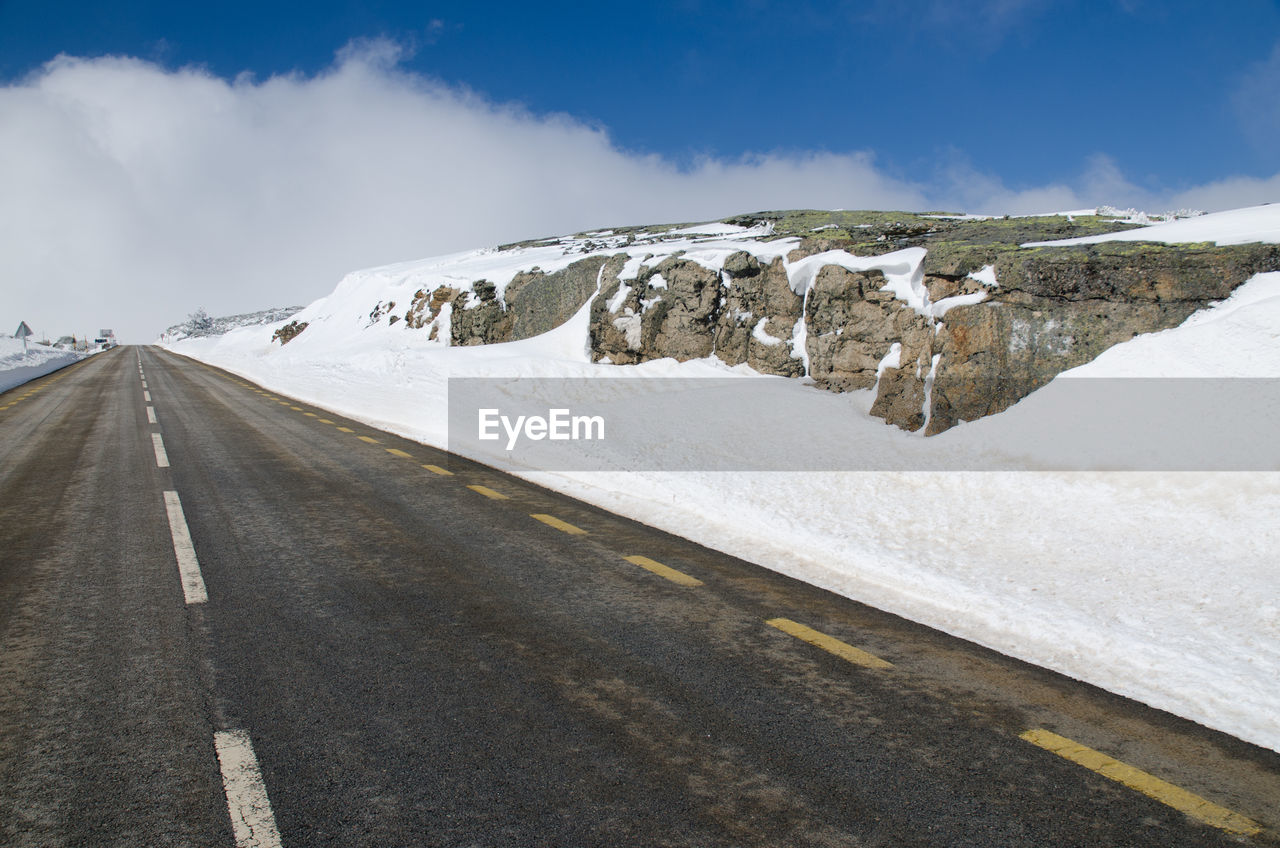 road, transportation, environment, snow, sky, landscape, cold temperature, winter, scenics - nature, mountain, travel, cloud, nature, beauty in nature, the way forward, travel destinations, no people, empty road, highway, symbol, land, mountain range, road marking, diminishing perspective, non-urban scene, asphalt, day, tourism, journey, snowcapped mountain, outdoors, marking, blue, remote, country road, vanishing point, sign, street, ice, tranquility, mountain pass, polar climate, frozen, tranquil scene, road trip, white, mode of transportation