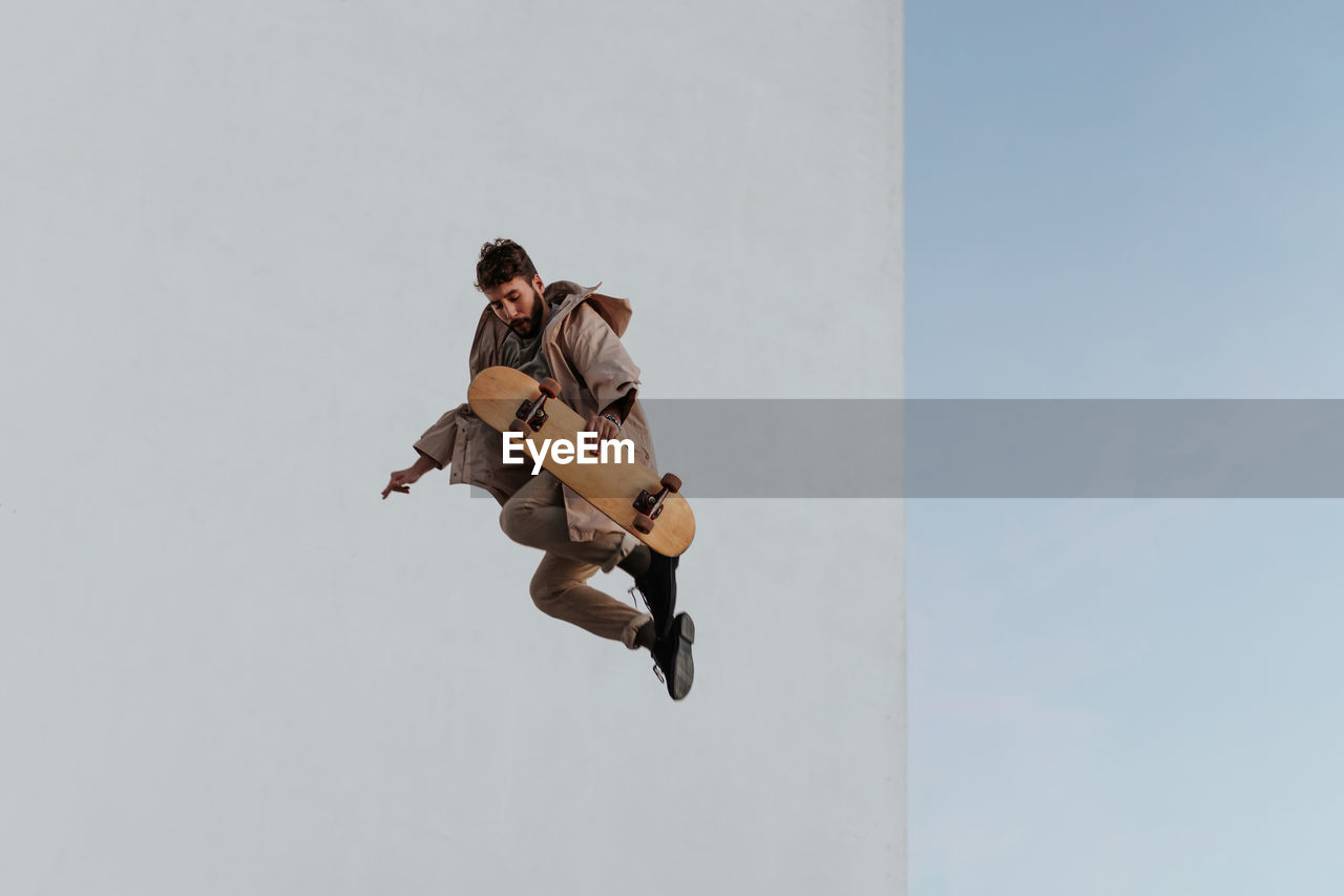 Full body young bearded active male skater in casual outfit jumping while performing trick on skateboard in skatepark