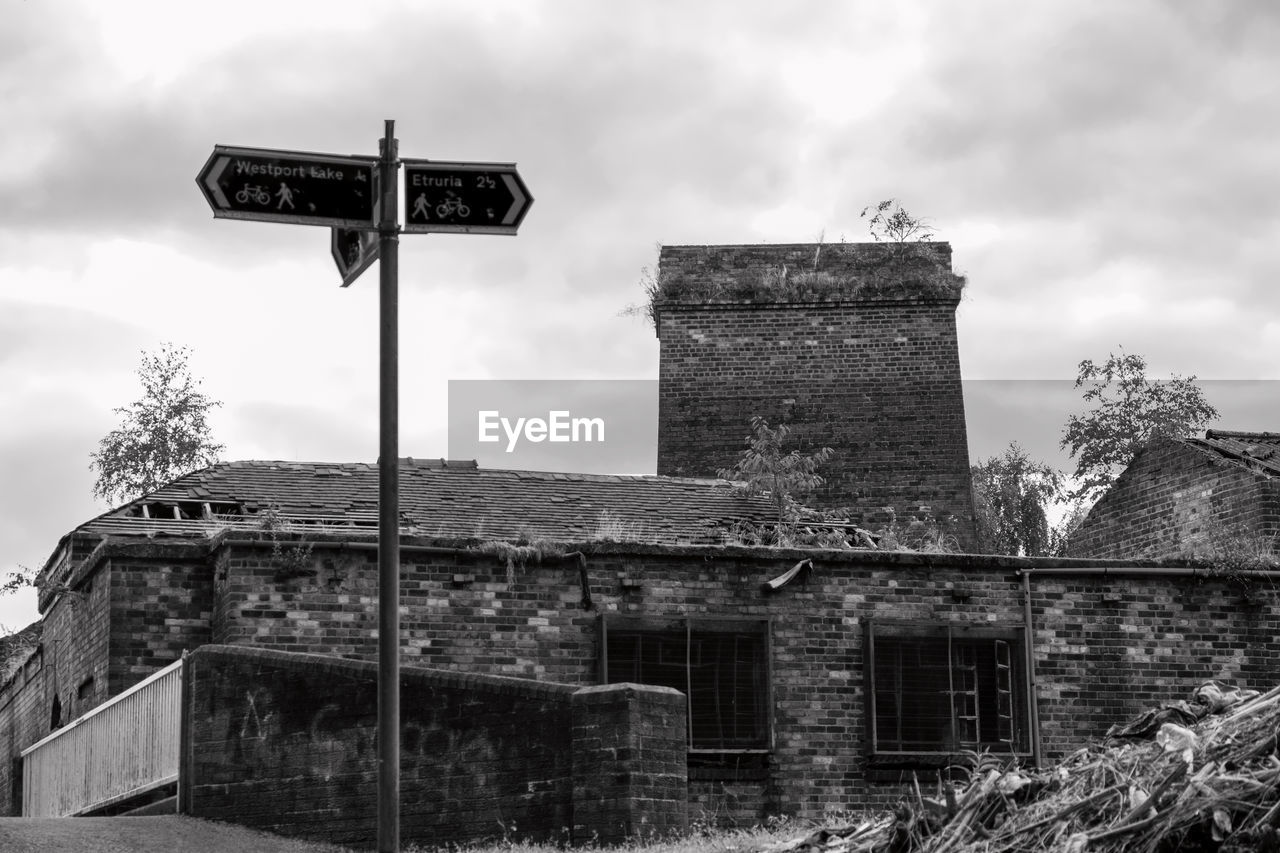 Directional sign by abandoned building against sky